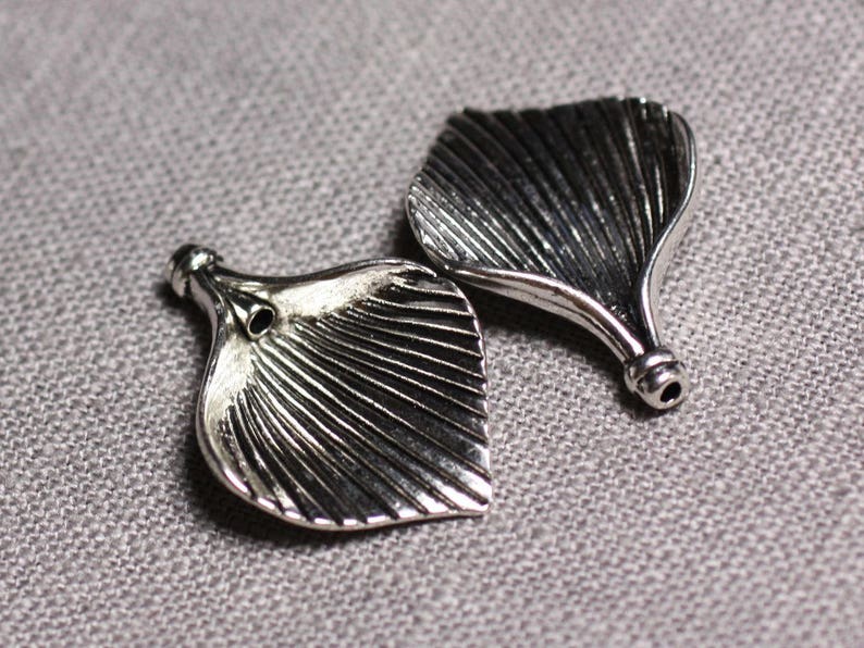 May include: Two silver metal leaf-shaped charms with a textured surface and a hole at the top.