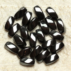 May include: A collection of black, smooth, polished, rectangular-shaped stones. The stones are arranged in a heart shape on a light beige fabric background.