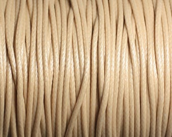 May include: Close-up of a spool of beige waxed cotton cord. The cord is tightly wound and has a smooth, polished finish.