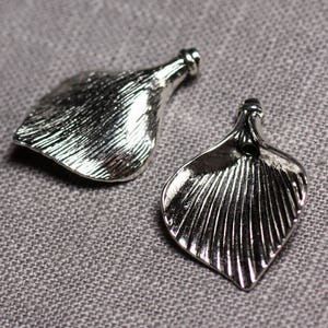 May include: Two silver metal flower-shaped charms with a textured surface. The charms have a hole at the top for attaching to a necklace or bracelet.