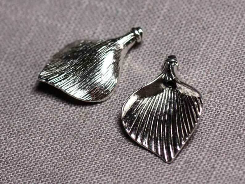May include: Two silver metal flower-shaped charms with a textured surface. The charms have a hole at the top for attaching to a necklace or bracelet.