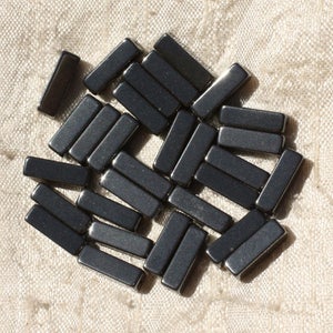 Peut inclure: Un groupe de perles rectangulaires noires, probablement en hématite, éparpillées sur un fond de tissu blanc.