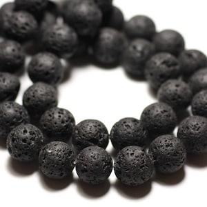 Peut inclure: Un fil de perles de roche volcanique noires. Les perles sont rondes avec une texture poreuse et sont disposées en cercle sur un fond blanc. Les perles sont de couleur charbon foncé.