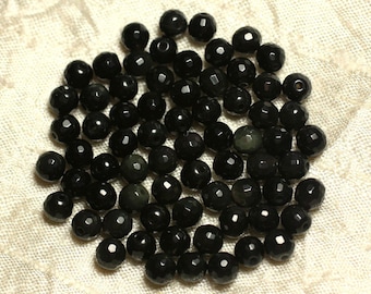 May include: A collection of black faceted beads, some with green flecks, arranged in a circular pattern on a white fabric background.