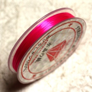 May include: A spool of vibrant pink crystal string, suitable for jewellery making. The spool has a clear plastic rim and a label with Japanese text and a red diamond design. The string is tightly wound and appears smooth and shiny.