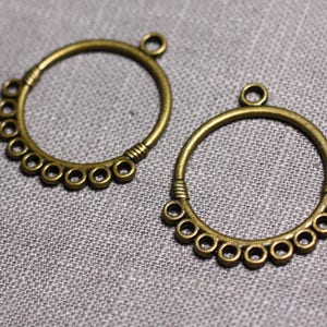 Puede incluir: Dos aros de metal de color dorado antiguo con una fila decorativa de pequeños círculos alrededor del perímetro. Los aros tienen un bucle en la parte superior para colgar.