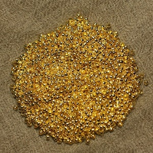 May include: A large pile of small, shiny gold beads. The beads are round and have a smooth, polished finish.