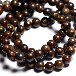 Peut inclure: Un collier de perles de pierres précieuses brun foncé. Les perles sont rondes et ont une texture légèrement rugueuse. Les perles sont enfilées sur un fil transparent.