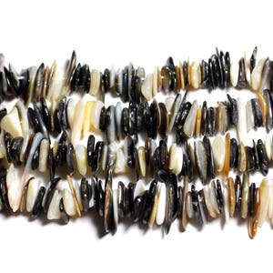 Può includere: Primo piano di diversi fili di perline di schegge di conchiglia naturale. Le perline sono un mix di colori nero, crema e beige. Le schegge hanno forma e dimensione irregolari, creando un aspetto strutturato. Le perline sono infilate, pronte per la creazione di gioielli.