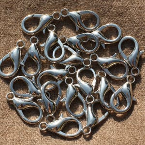 Peut inclure: Gros plan sur des fermoirs mousquetons argentés, disposés sur un fond marron texturé. Ces fermoirs, avec leur mécanisme à ressort, sont parfaits pour la création de bijoux et divers projets d'artisanat. Chaque fermoir mesure environ 2,5 cm de long.