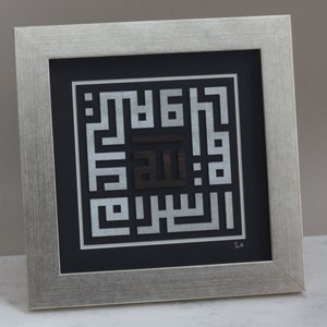 May include: A framed silver and black Islamic calligraphy art piece with the Arabic word "Allah" in the center. The artwork is framed in a silver frame with a black mat.