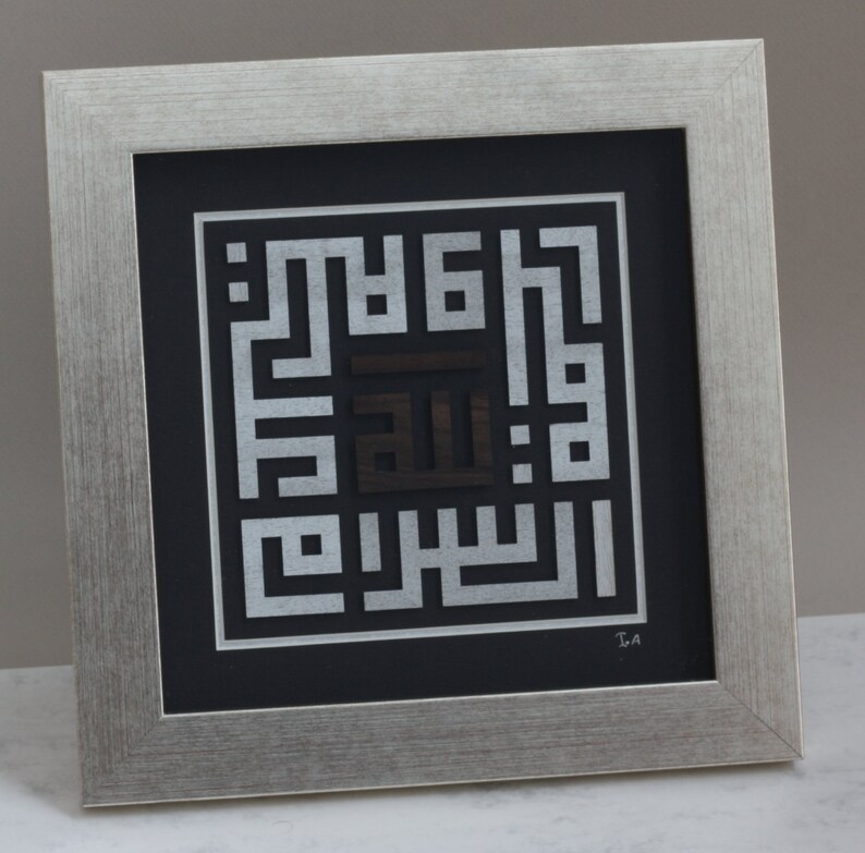 May include: A framed silver and black Islamic calligraphy art piece with the Arabic word "Allah" in the center. The artwork is framed in a silver frame with a black mat.