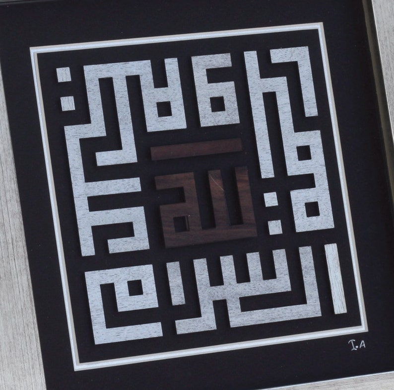 May include: A framed artwork featuring a silver and brown wood calligraphy piece with the Arabic word "Allah" in the center. The artwork is framed in a black and silver frame.