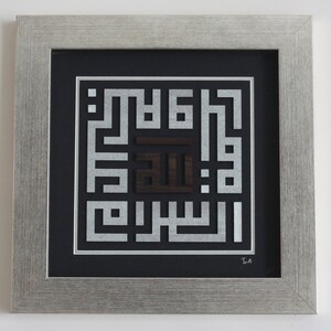 May include: A framed artwork featuring a silver and black Islamic calligraphy design. The design is made up of intricate geometric patterns and the word "Allah" is prominently displayed in the center.