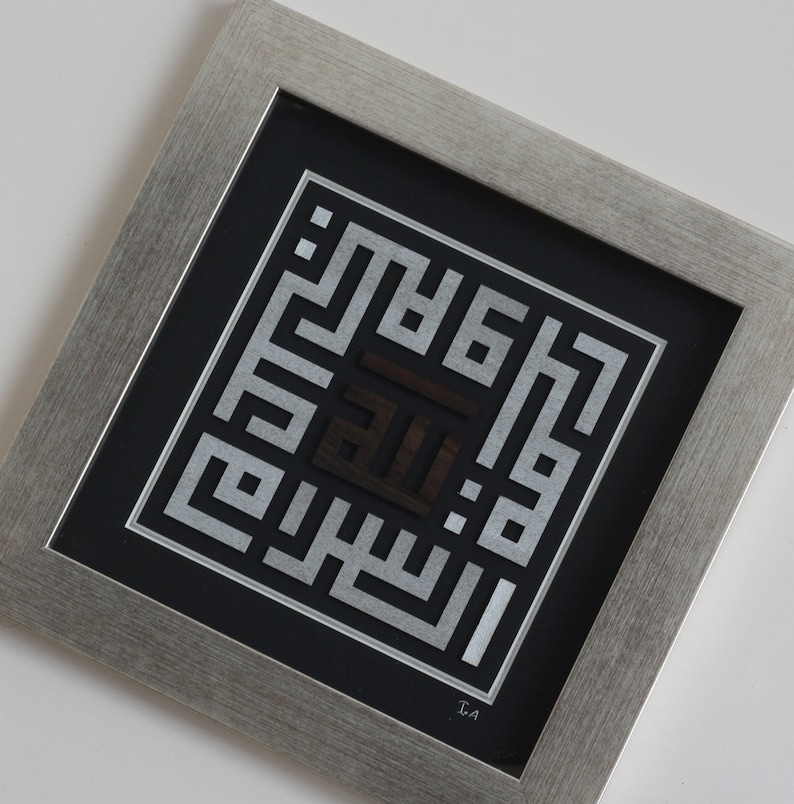 May include: A framed silver and black Islamic calligraphy art piece with the word "Allah" in the center. The artwork is framed in a silver frame with a black mat.