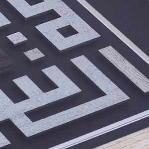 May include: A close-up of a framed artwork with a geometric design in white and gray. The design is made of layered squares and rectangles, creating a 3D effect.
