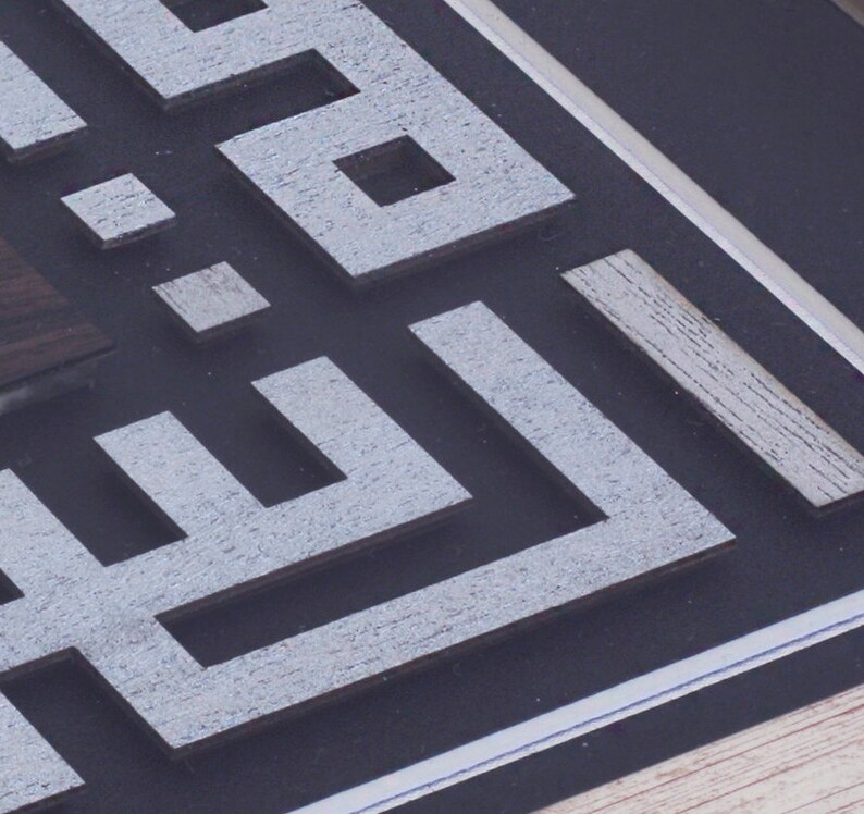 May include: A close-up of a framed artwork with a geometric design in white and gray. The design is made of layered squares and rectangles, creating a 3D effect.