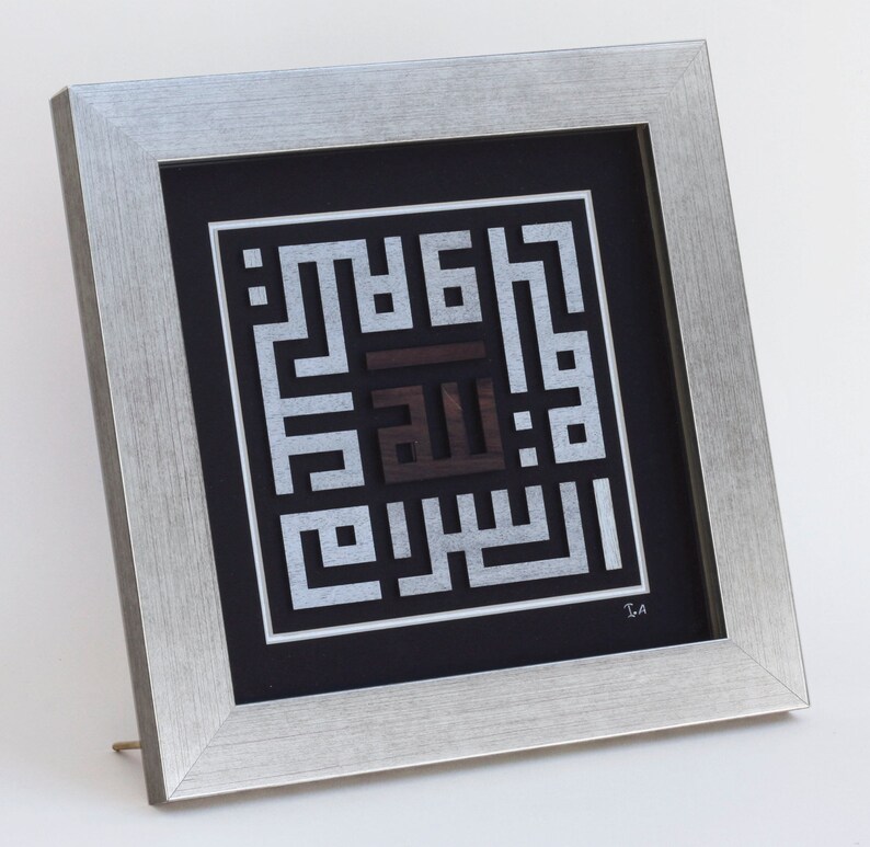 May include: A framed silver and black Islamic calligraphy artwork with the Arabic word "Allah" in the center. The artwork is framed in a silver frame with a black mat.