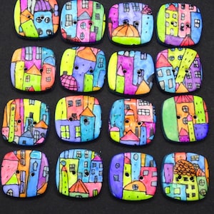 Puede incluir: Dieciséis botones cuadrados con esquinas redondeadas, cada uno con una ilustración pintada a mano de un paisaje urbano con casas en tonos rosa, azul, verde, naranja y morado. Cada botón tiene dos agujeros centrales y el texto Boutons d'Ay.