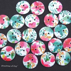 May include: A collection of round, two-hole buttons featuring a white base with a colourful floral pattern of pink flowers, green leaves, and small orange berries. The text "Boutons d'Auj'" is printed in white in the bottom left corner of the image.