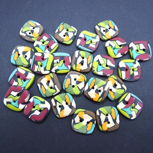 Puede incluir: Una colección de veintiún botones cuadrados, cada uno con un patrón abstracto multicolor en tonos verde lima, turquesa, granate, blanco y tostado. Cada botón tiene dos orificios centrales para su fijación y esquinas redondeadas.
