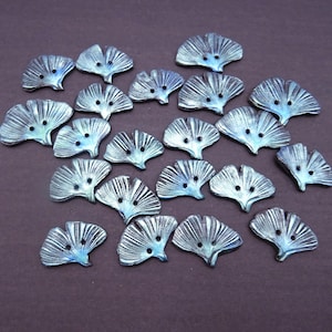 Peut inclure: Un ensemble de vingt-deux boutons en forme de feuille de ginkgo avec une finition métallique bleue et argentée. Chaque bouton présente une forme d'éventail avec des stries rayonnantes et deux petits trous au centre pour la fixation.
