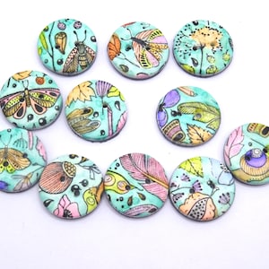 Peut inclure: Un ensemble de dix boutons ronds présentant un fond turquoise vif avec des illustrations colorées de papillons, de plumes, de feuilles et d'éléments floraux. Chaque bouton possède deux petits trous au centre pour la fixation sur tissu.