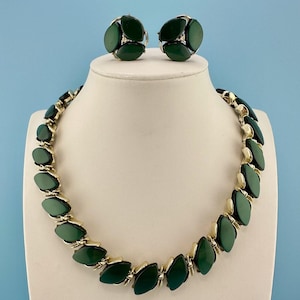 May include: A jewelry set consisting of a necklace and a pair of clip-on earrings. The necklace features a series of dark green, marquise-shaped cabochons set in gold-tone metal links. The matching earrings feature a cluster of three green cabochons.