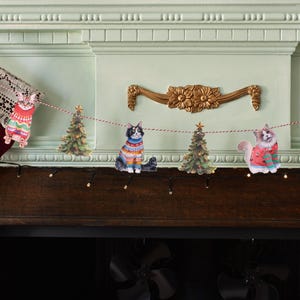 以下が含まれることがあります： カラフルな柄のセーターを着た猫と緑のクリスマスツリーの切り抜きが交互に並ぶ装飾用ガーランド。フィギュアは細いねじれた紐でつながれており、ホリデーシーズンをテーマにした華やかなディスプレイを作り出しています。