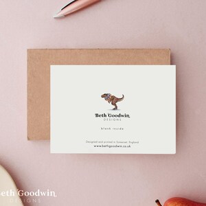 May include: A white card with a cartoon illustration of a Tyrannosaurus Rex wearing a colorful flower garland. The text "Beth Goodwin, DESIGNS" is below the illustration. The text "blank inside" is below the logo. The text "Designed and printed in Somerset, England" is below the text "blank inside". The text "www.bethgoodwin.co.uk" is below the text "Designed and printed in Somerset, England".