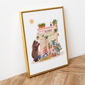 Op de afbeelding: Een aquarelillustratie van een roze winkelgevel met de woorden "Bloom Flowers & Coffee" boven de deur. Een bruine beer staat buiten de winkel en kijkt naar de deur. De winkel heeft een bord met de tekst "Open" en een welkommat met de tekst "Come On In".