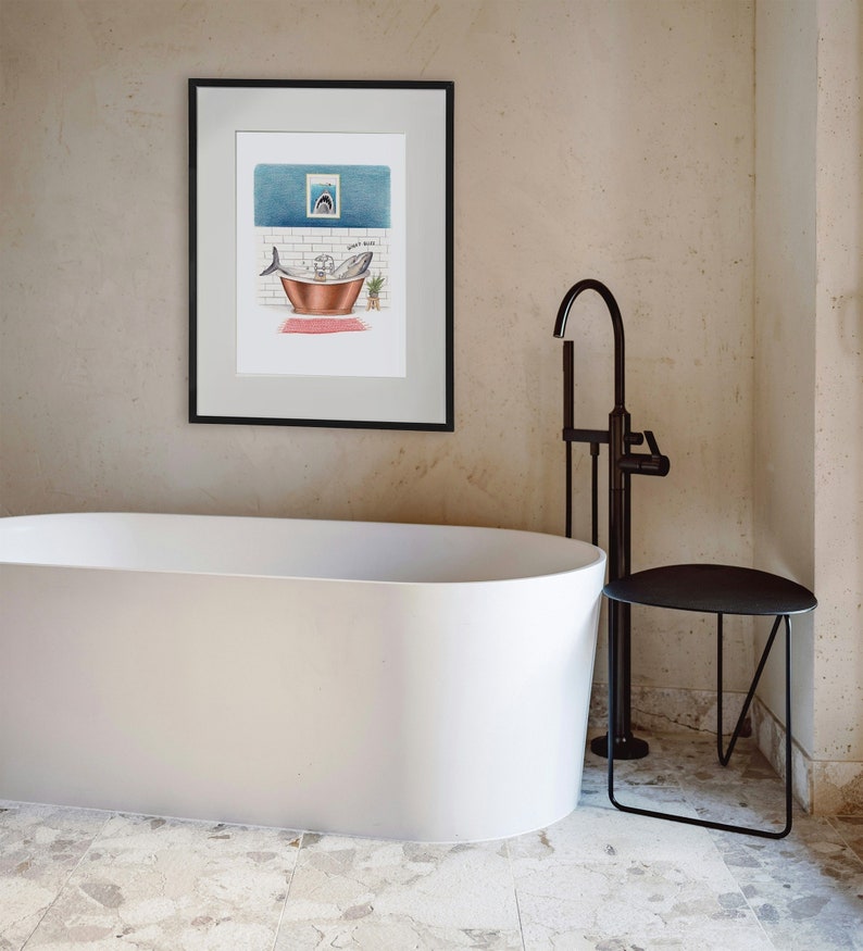 May include: A white bathtub with a black faucet and a black side table. A framed illustration of a shark in a bathtub with the text "Don't Panic" is hanging on the wall.