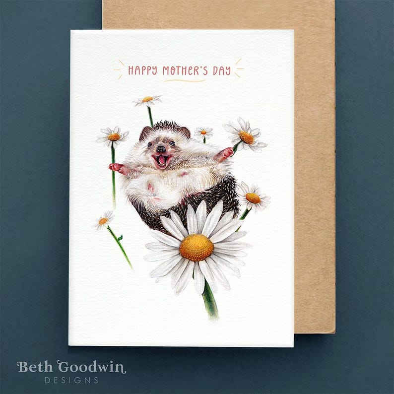 K&ouml;nnte beinhalten: Eine Gru&szlig;karte mit einer Aquarell-Illustration eines fr&ouml;hlichen Igels, der auf einer G&auml;nsebl&uuml;mchen sitzt. Die Karte lautet "Happy Mother's Day" in rosa Schrift.