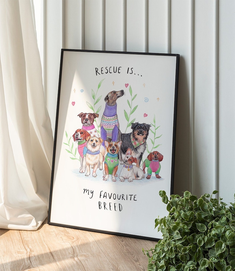 May include: A white framed print with a hand-drawn illustration of seven dogs wearing colorful sweaters. The text "RESCUE IS... my FAVORITE BREED" is written below the dogs.