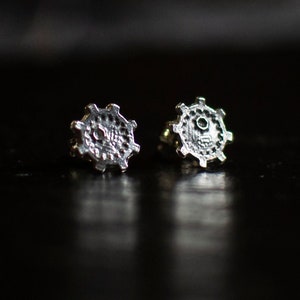 May include: A pair of silver earrings with a detailed, circular design. The earrings are on a black surface.