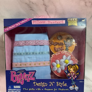 Puede incluir: Un set Bratz Design 'N' Style en caja. El set incluye una almohada azul claro con ribetes rosas y elementos decorativos. La caja presenta el texto "Pillow Perfect" y "The girls with a Passion for Fashion!"