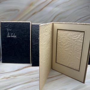 May include: A set of three photo frames. The frames are black and beige with textured surfaces. The text "Portrait by Don Tucker" is visible on the black frame.