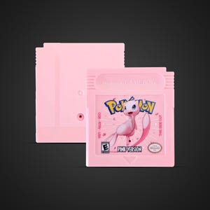 Könnte beinhalten: Eine rosa Nintendo Game Boy-Cartridge mit der Aufschrift "Pink Version". Die Cartridge zeigt den Pokémon-Charakter Mew mit dem Pokémon-Logo darüber. Der Text "THIS SIDE OUT" ist auf der rechten Seite sichtbar.