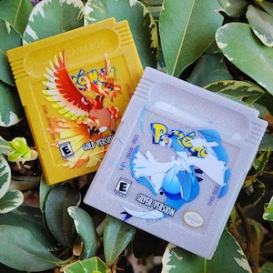 May include: Two Game Boy cartridges: a gold cartridge with a fiery bird graphic labeled "Gold Version" and a silver cartridge with a blue and white creature graphic labeled "Silver Version". Both cartridges have the "E" rating.