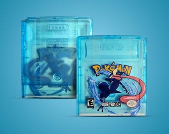 May include: A translucent blue Game Boy Color video game cartridge titled Pokémon Blue Version. The front label features a dark blue character with a long pink tongue surrounded by water splashes, the Pokémon logo, and an ESRB E rating symbol.