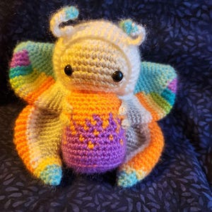 May include: A crocheted butterfly toy with a white head, orange and purple body, and rainbow wings.