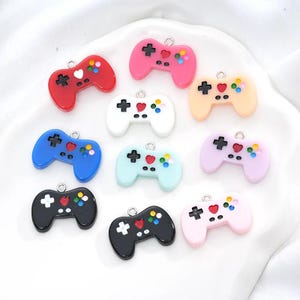 May include: A selection of colourful video game controller charms in shades of red, pink, blue, white, black, and pastels. Each charm features a cross, heart, and colourful buttons, with a small loop for attaching to jewellery or crafts.