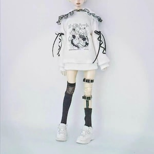 May include: A white sweatshirt with a black and white graphic print and Japanese text. The sweatshirt has a black lace collar and black ribbons on the sleeves. The doll is wearing black thigh-high socks, black leg straps, and white trainers.