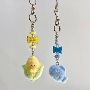 May include: Two handmade phone charms. One features a yellow corn character with green leaves, the other a blue whale. Both have silver chains, clear and yellow beads, and a yellow charm that says "Sweet".