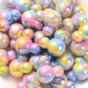 May include: A collection of iridescent, Mickey Mouse-shaped beads in various sizes. The beads have a pearlescent finish with colors including pink, yellow, blue, and green. These decorative beads are ideal for crafting and jewelry making.