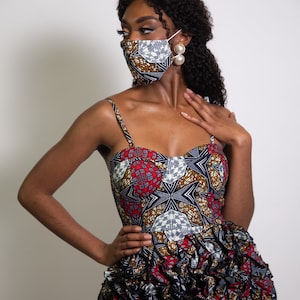 May include: A woman wearing a black and white patterned face mask with a red and gold patterned dress. The dress has a ruffled skirt.