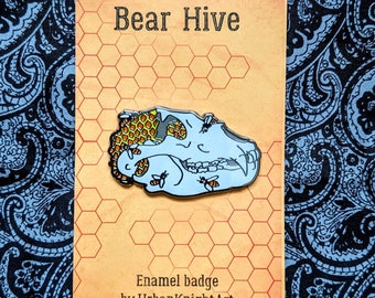 Può includere: Uno spillo in smalto blu chiaro con un design a forma di teschio d'orso. Il teschio è ricoperto da un motivo a nido d'ape con accenti gialli e arancioni. Lo spillo dice "Bear Hive" e "Enamel badge by UrbanKnightArt".