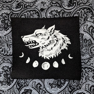 Peut inclure: Patch brodé noir et blanc d'une tête de loup avec une lune croissante et des phases de pleine lune autour du cou.
