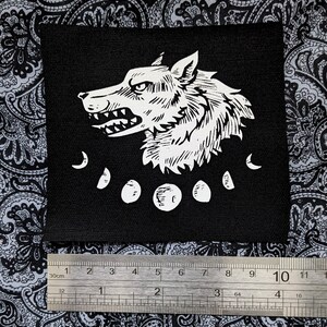 May include: Black and white iron-on patch featuring a wolf's head with a snarling expression and five crescent moons.