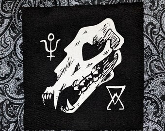 May include: Black and white embroidered patch featuring a skull with sharp teeth, a symbol of the planet Uranus, and a pentagram. The patch is on a black fabric background.